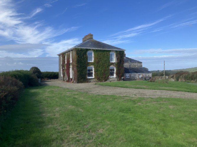 The front elevation of Hendre farmhouse, a stone house clad in ivy with a slate roof, seen across the lawn and gravel drive under a bright blue sky.